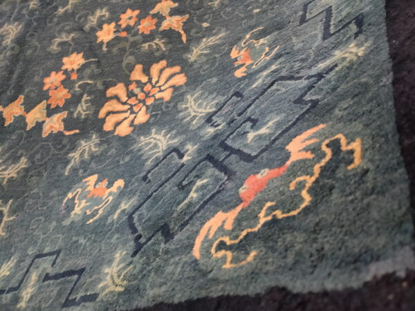 Blue-green rug with scattered peach florals and dark blue geometric line patterns.