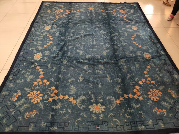 Deep teal rug with a sheen, featuring apricot floral patterns and a dark geometric border on light tile.
