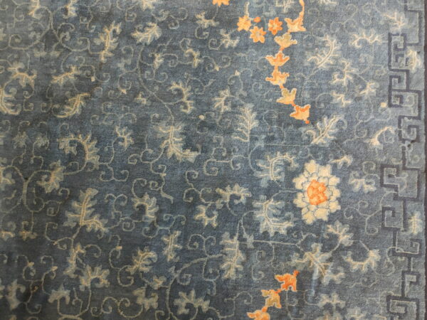 Blue high-density rug showing muted floral patterns, apricot accents, and a dark geometric border.