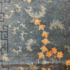 Textured blue rug displaying orange flowers, ivory vines, and a dark blue Greek key border pattern.