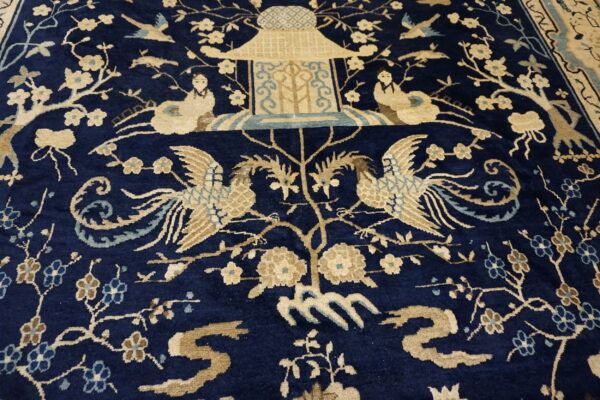 Navy blue rug with a dense pattern of tan birds, figures, flowers, and a central pavilion.