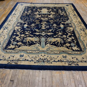 Blue and tan large rug featuring detailed landscape and animal motifs displayed on aged wood flooring.