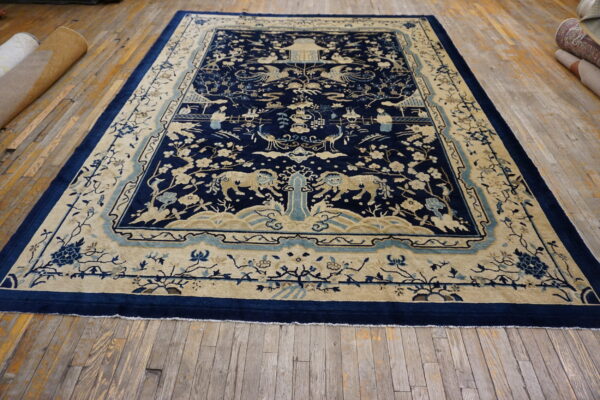 Blue and tan large rug featuring detailed landscape and animal motifs displayed on aged wood flooring.