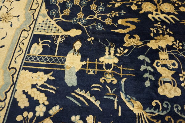Close-up of a navy rug field with tan and sage pictorial elements, including a figure, flowers, and a bird.