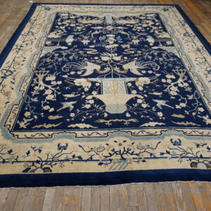Large, deep blue rug featuring cream birds and florals, laid over rustic light brown wood flooring.