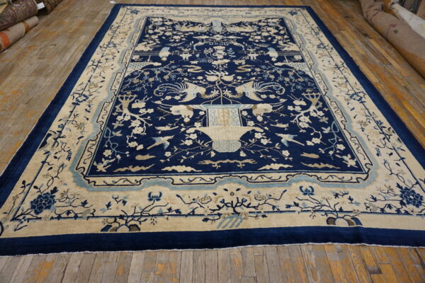 Large, deep blue rug featuring cream birds and florals, laid over rustic light brown wood flooring.