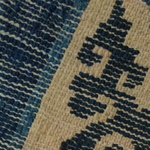 Overlapping rugs feature a dark blue patterned texture next to a tight-weave beige and blue geometric design.