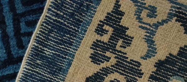 Overlapping rugs feature a dark blue patterned texture next to a tight-weave beige and blue geometric design.