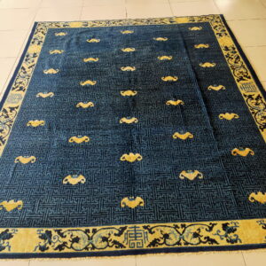 Blue key-pattern rug with yellow bat motifs and a wide floral border on light tile floor.