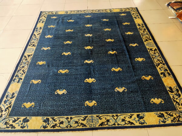 Blue key-pattern rug with yellow bat motifs and a wide floral border on light tile floor.