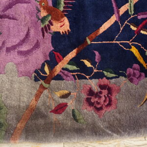 Close-up of a high-pile rug featuring a colorful bird, branch, and flower design on navy and purple fields.
