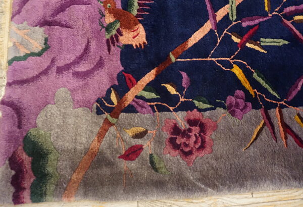 Close-up of a high-pile rug featuring a colorful bird, branch, and flower design on navy and purple fields.