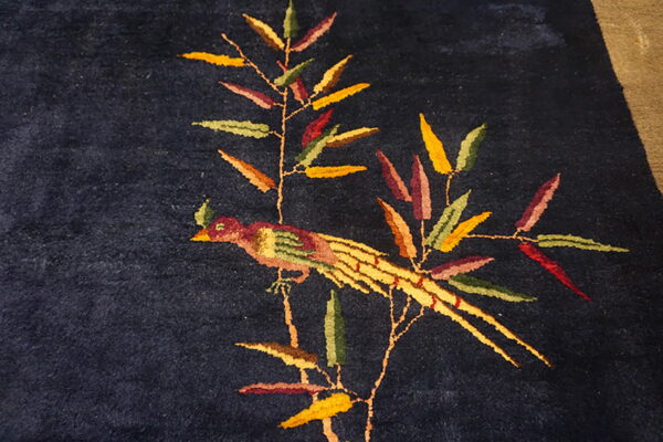 Dark blue pile rug featuring a decorative motif of a colorful bird perched on a leafy branch.