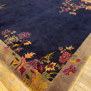 Close up of a velvety navy rug with a multicolored botanical pattern and taupe border on wooden planks.