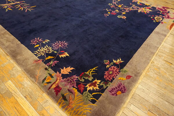 Close up of a velvety navy rug with a multicolored botanical pattern and taupe border on wooden planks.