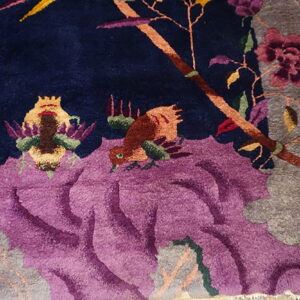 Detailed view of a navy carved rug with purple flowers, gray accents, and colorful bird patterns.