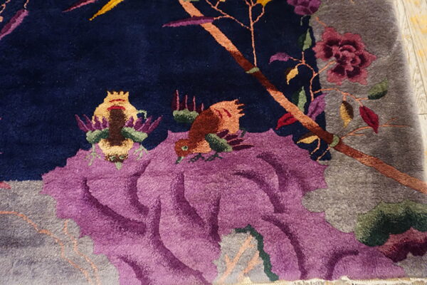 Detailed view of a navy carved rug with purple flowers, gray accents, and colorful bird patterns.