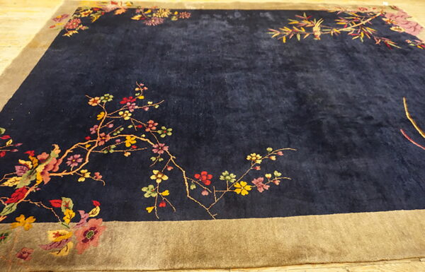 Dark blue high-pile rug featuring multicolored floral branches and a wide tan border.