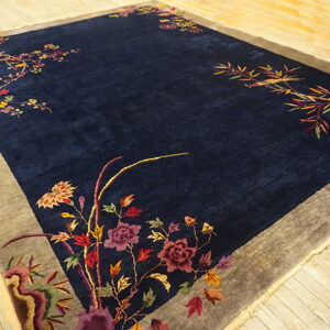 Deep blue rug featuring ornate multicolored floral vines along the edges and a wide gray border on wood flooring.