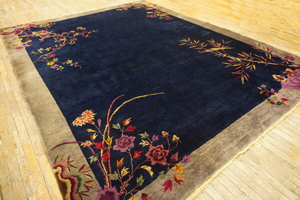 Deep blue rug featuring ornate multicolored floral vines along the edges and a wide gray border on wood flooring.