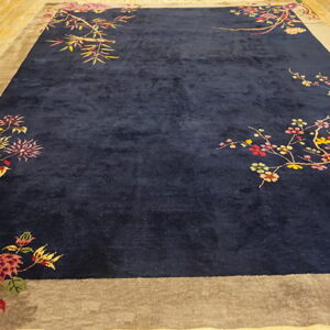 Plush navy rug with a taupe border and colorful floral and branch designs on wood flooring.