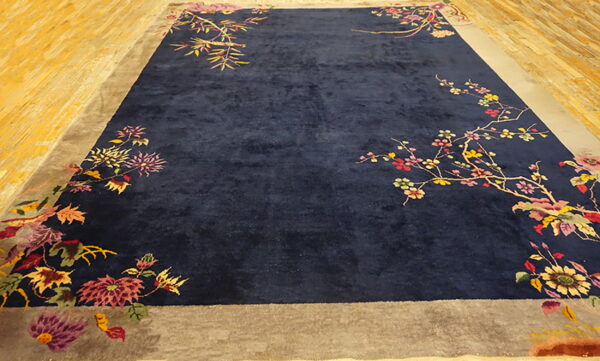 Plush navy rug with a taupe border and colorful floral and branch designs on wood flooring.