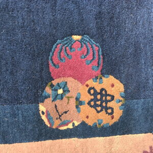 Detailed view of a dark blue rug with stacked magenta and tan circular motifs and contrasting accents.