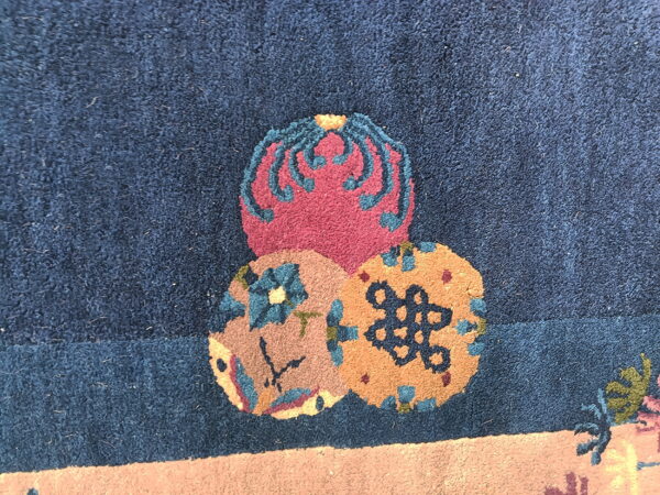 Detailed view of a dark blue rug with stacked magenta and tan circular motifs and contrasting accents.