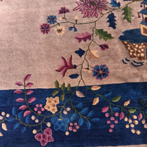Plush rug detail showing a taupe field, a deep blue border, and colorful magenta and blue floral motifs.