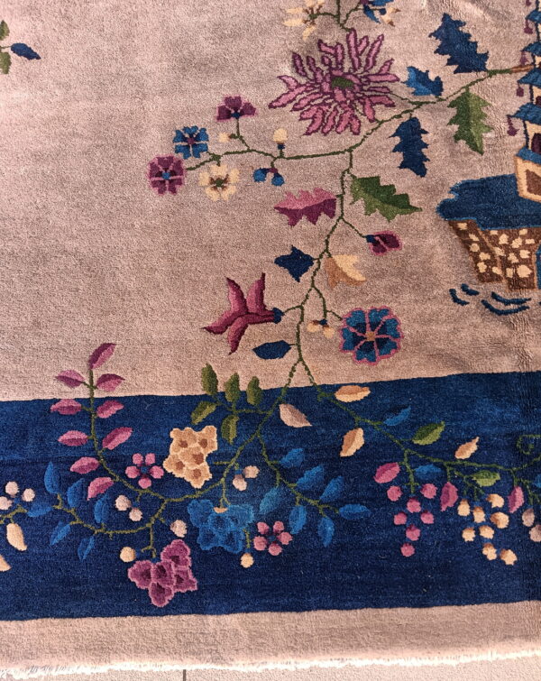 Plush rug detail showing a taupe field, a deep blue border, and colorful magenta and blue floral motifs.