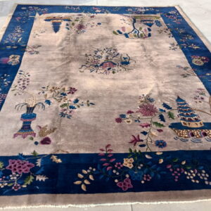 A large rug with a central beige field and scattered Chinoiserie floral patterns, surrounded by a broad indigo border.