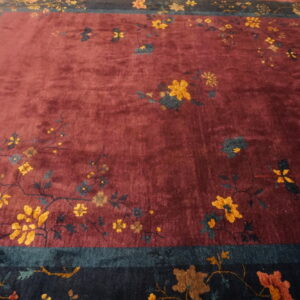 A maroon rug with a deep pile features scattered gold and blue floral patterns, bordered by thick navy and teal bands.