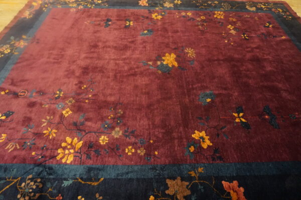 A maroon rug with a deep pile features scattered gold and blue floral patterns, bordered by thick navy and teal bands.