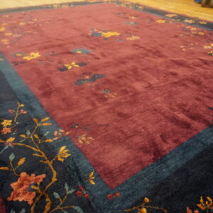 High-pile burgundy rug with scattered flowers and a contrasting dark teal border on wood planks.
