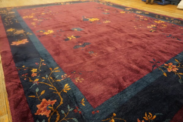 High-pile burgundy rug with scattered flowers and a contrasting dark teal border on wood planks.