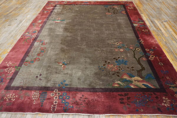 Large rug featuring a gray field with subtle motifs and a wide crimson border, resting on wood floorboards.