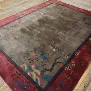 Gray rug with a large multicolored floral design and wide maroon border rests on distressed yellow wood planks.