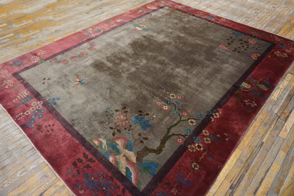 Gray rug with a large multicolored floral design and wide maroon border rests on distressed yellow wood planks.