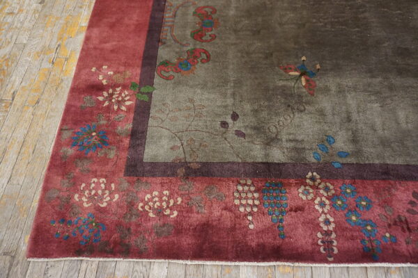Distressed green and red floral rug with a dark border resting on weathered wood plank floors.