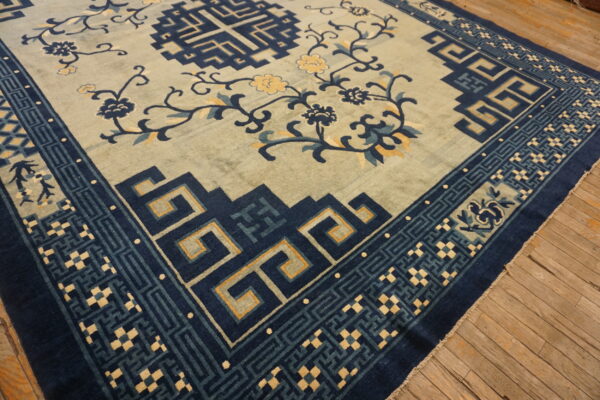 A sage green rug featuring scrolling floral designs and dark blue geometric borders on rustic wood floors.