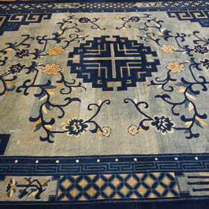 Blue and indigo rug featuring a geometric fretwork border, central motif, and gold floral designs on a muted field.