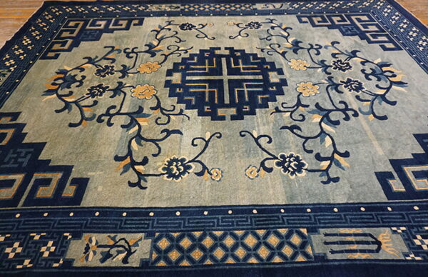 Blue and indigo rug featuring a geometric fretwork border, central motif, and gold floral designs on a muted field.