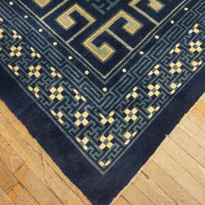 Dark blue rug corner with contrasting light blue and cream geometric border on rustic hardwood planks.