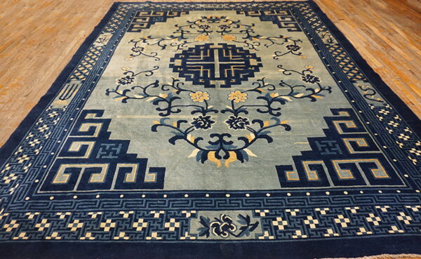 Slate blue rug featuring navy blue geometric designs, yellow floral accents, and wide plank hardwood flooring.