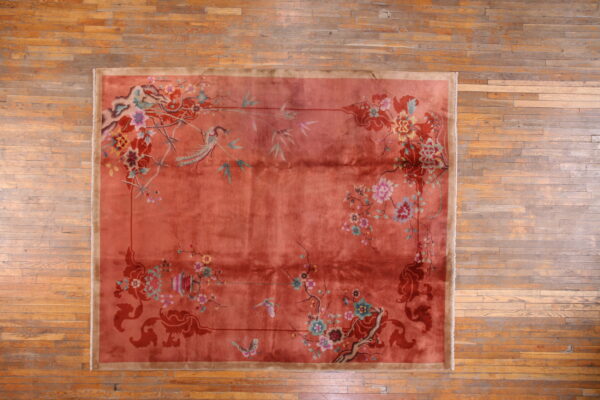 Low-pile rose rug featuring detailed multicolored birds and flowers rests on aged plank wood flooring.