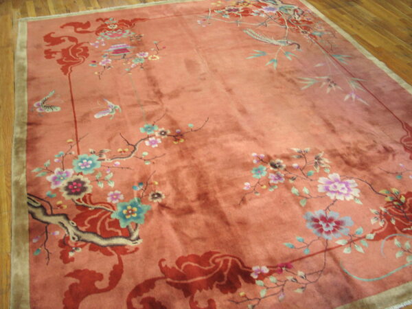 Plush, shaded salmon rug featuring detailed botanical, bird, and butterfly designs over wooden floorboards.