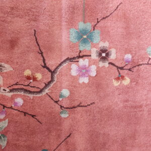 Close-up of a pink pile rug featuring a brown branch with green, pink, and multicolored floral motifs.