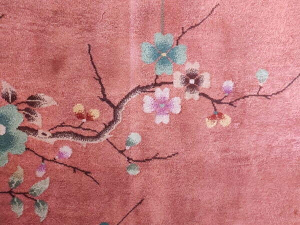 Close-up of a pink pile rug featuring a brown branch with green, pink, and multicolored floral motifs.