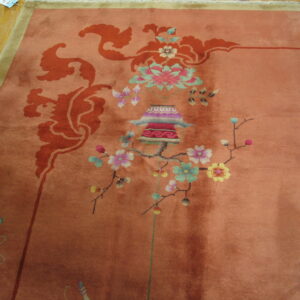 Rose-colored rug with intricate multi-color floral, lantern, and butterfly motifs rests on wood flooring.