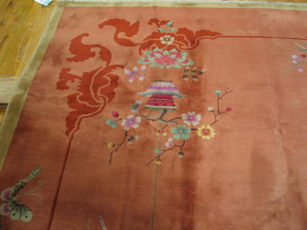 Rose-colored rug with intricate multi-color floral, lantern, and butterfly motifs rests on wood flooring.